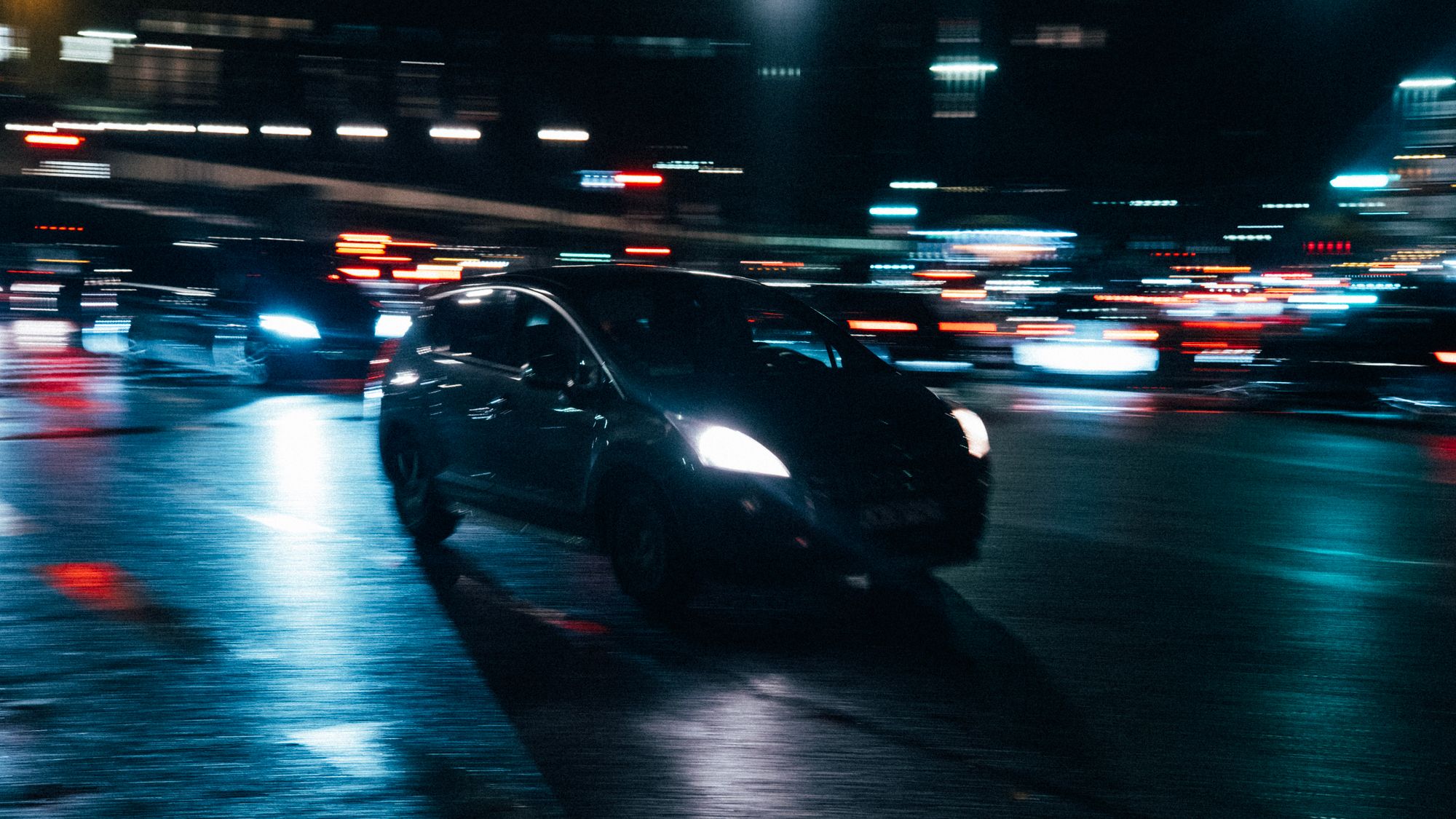 Stock photo: a dark sedan on a wet city street at night, neon lights streaking past